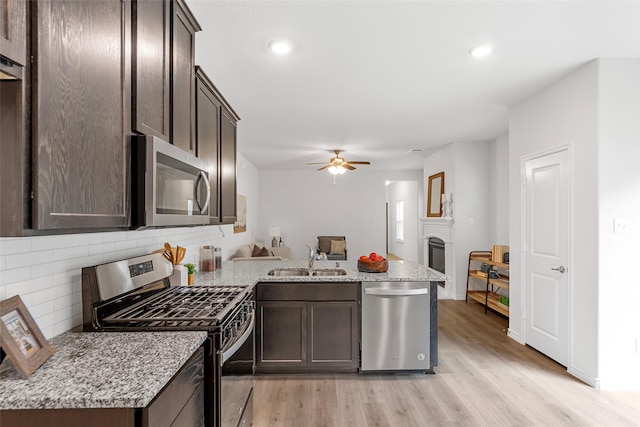 kitchen featuring dark brown cabinetry, a sink, light wood-style flooring, stainless steel appliances, and a peninsula