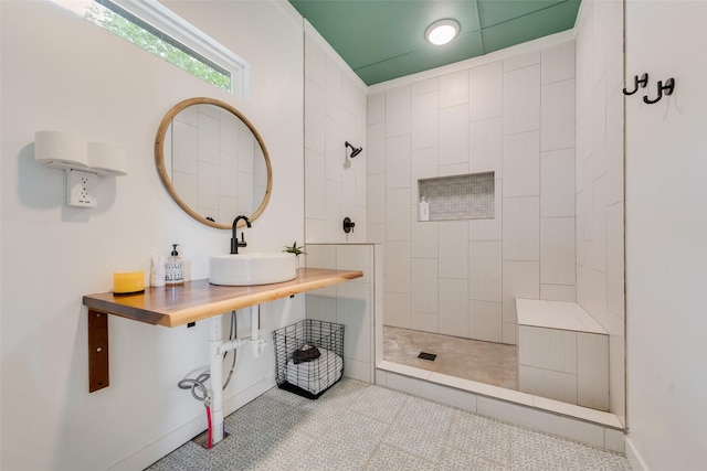 bathroom with baseboards, a sink, tile patterned floors, and a tile shower