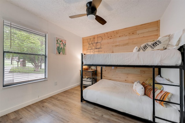 bedroom with a textured ceiling, wood finished floors, wooden walls, and multiple windows