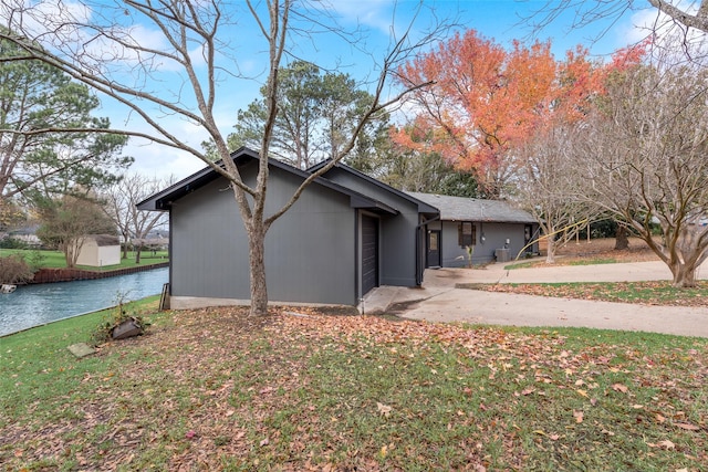 view of home's exterior with a garage, a water view, a yard, and concrete driveway