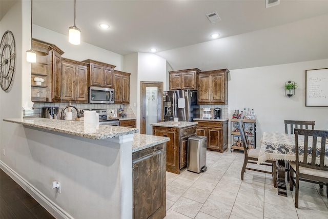 kitchen with light stone countertops, appliances with stainless steel finishes, backsplash, a center island, and a peninsula