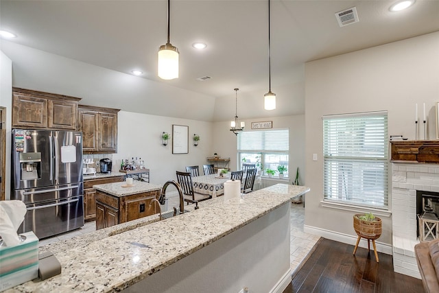 kitchen featuring light stone counters, a sink, visible vents, a center island, and stainless steel fridge