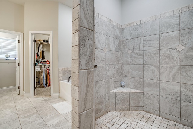 full bathroom featuring a garden tub, a spacious closet, and tiled shower
