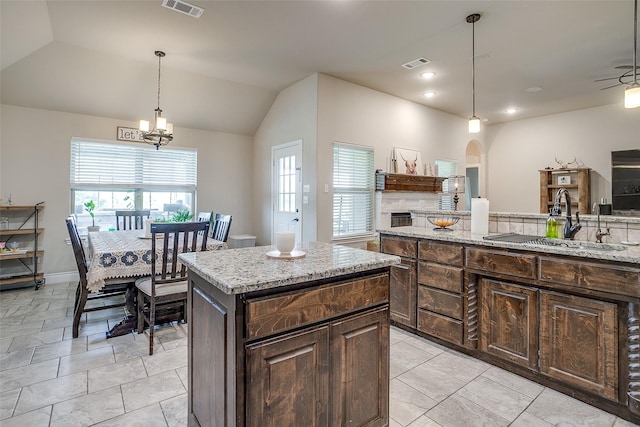 kitchen with a sink, visible vents, a kitchen island, arched walkways, and vaulted ceiling