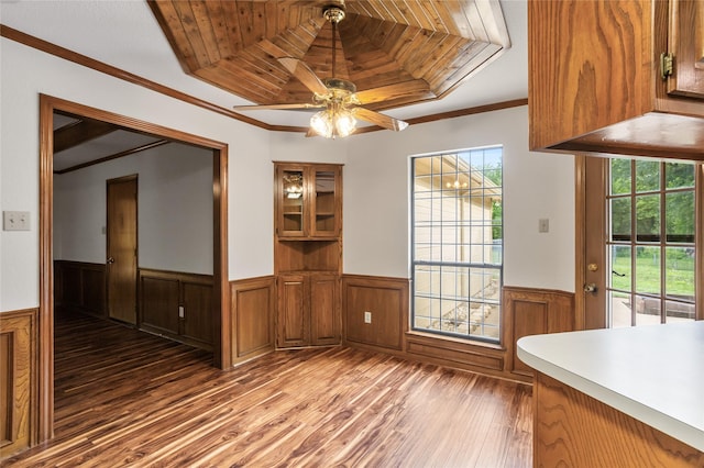unfurnished dining area featuring wainscoting, ornamental molding, light wood-type flooring, and a raised ceiling