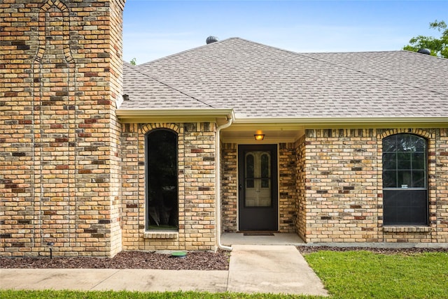 view of exterior entry featuring brick siding and a shingled roof