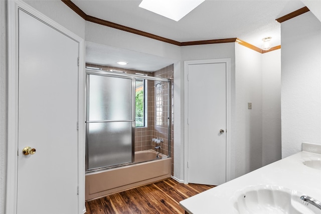 bathroom featuring wood finished floors, combined bath / shower with glass door, double vanity, a sink, and crown molding