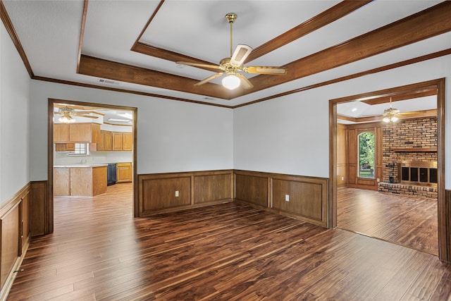 unfurnished living room with a raised ceiling, a ceiling fan, visible vents, hardwood / wood-style floors, and wainscoting