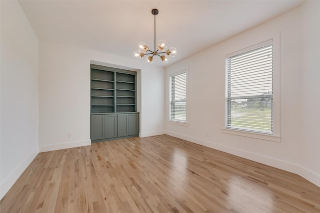 unfurnished room featuring an inviting chandelier, baseboards, and light wood-type flooring