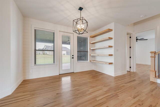 unfurnished dining area with baseboards, an inviting chandelier, and light wood-style flooring