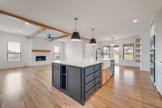 kitchen with open shelves, appliances with stainless steel finishes, a sink, a fireplace, and light wood-type flooring