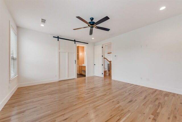 interior space featuring a barn door, a ceiling fan, baseboards, light wood-type flooring, and visible vents