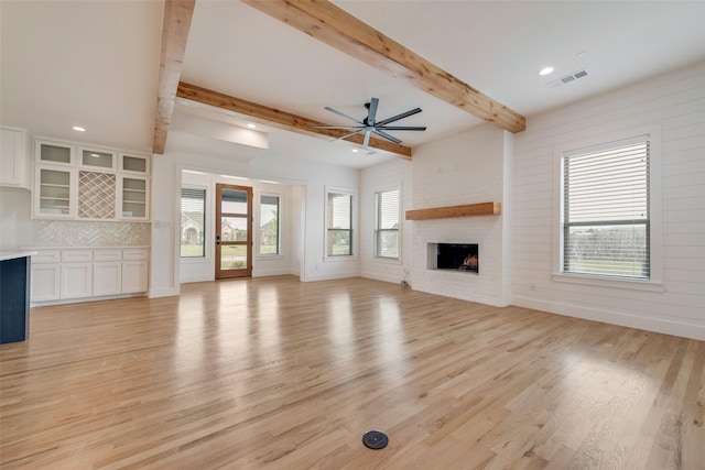 unfurnished living room with a wealth of natural light, light wood finished floors, ceiling fan, and visible vents