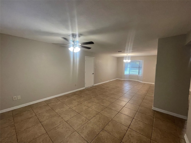 tiled empty room featuring baseboards and ceiling fan with notable chandelier