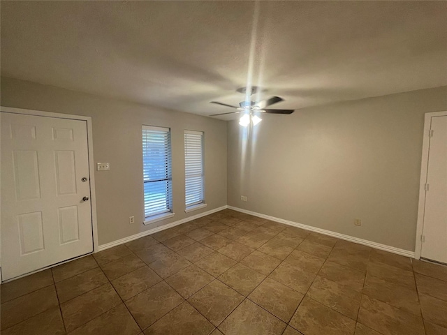 empty room featuring tile patterned floors, a ceiling fan, and baseboards