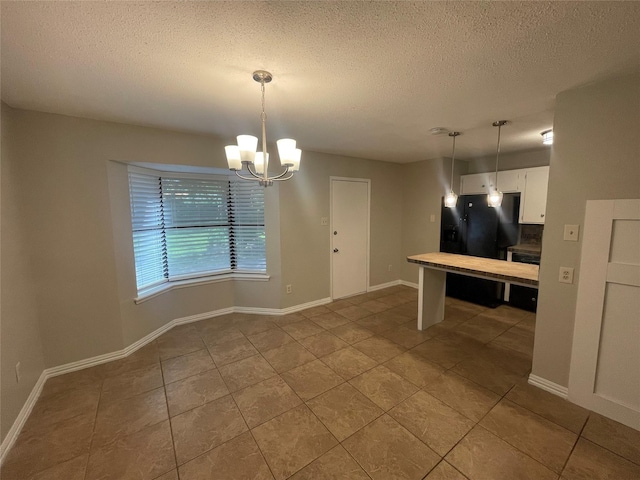 unfurnished dining area featuring a textured ceiling, an inviting chandelier, tile patterned floors, and baseboards