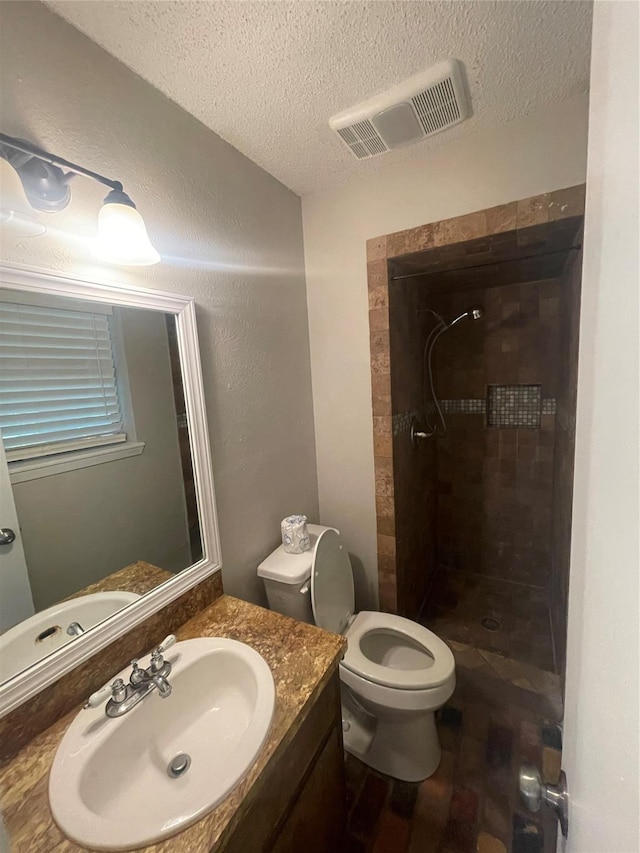 bathroom with vanity, toilet, a tile shower, visible vents, and a textured ceiling