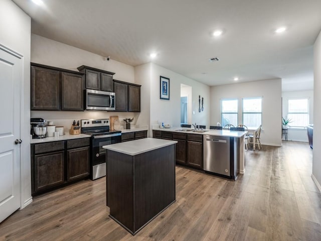 kitchen with a peninsula, appliances with stainless steel finishes, wood finished floors, and light countertops