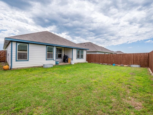 back of house with a yard, a shingled roof, and a fenced backyard
