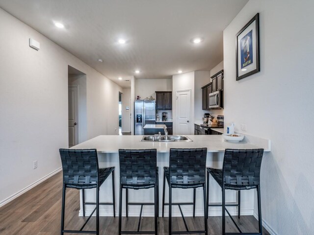 kitchen featuring dark wood finished floors, stainless steel appliances, a sink, a peninsula, and a kitchen breakfast bar