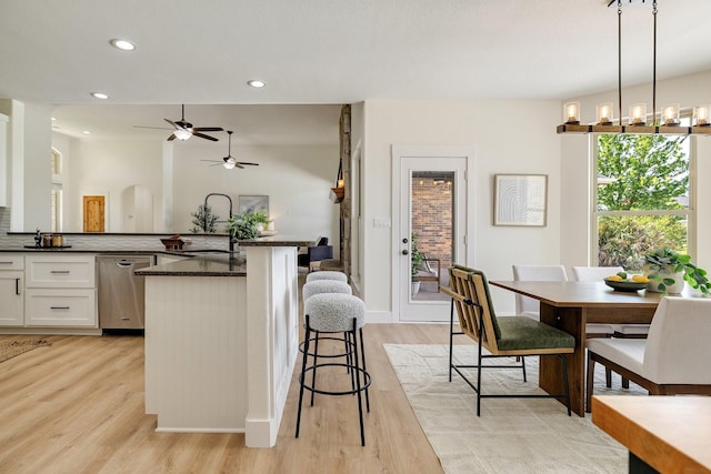 kitchen featuring stainless steel dishwasher, light wood-style flooring, ceiling fan, a kitchen bar, and white cabinetry