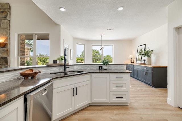 kitchen with dark stone countertops, stainless steel dishwasher, plenty of natural light, and a sink