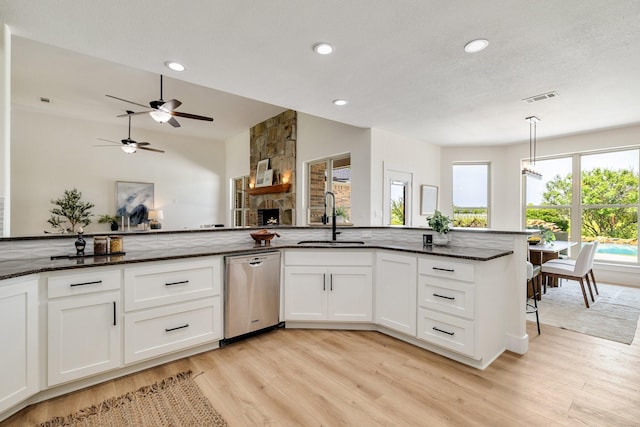 kitchen featuring dark stone countertops, stainless steel dishwasher, a sink, light wood-type flooring, and a stone fireplace