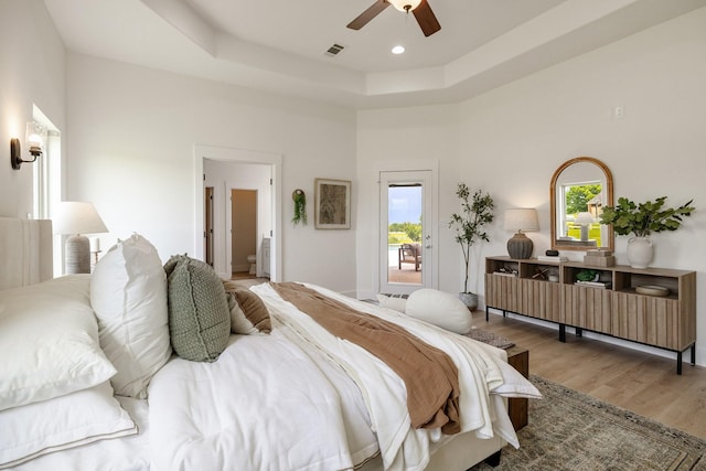 bedroom featuring ceiling fan, a tray ceiling, recessed lighting, wood finished floors, and access to outside