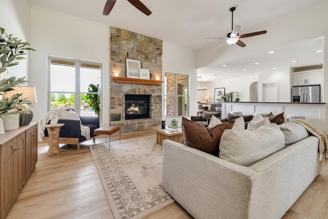 living area featuring a high ceiling, light wood finished floors, a ceiling fan, and a fireplace