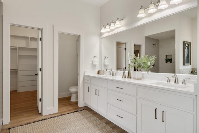 full bath with toilet, double vanity, a sink, and wood finished floors