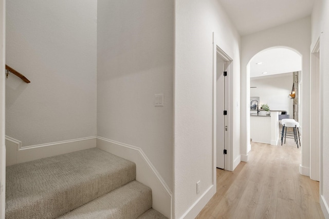 hallway with baseboards, arched walkways, stairs, and light wood-style flooring