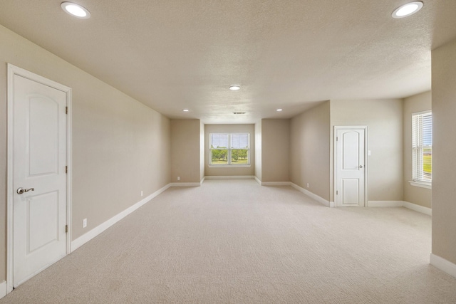 empty room with a textured ceiling, recessed lighting, baseboards, and light carpet