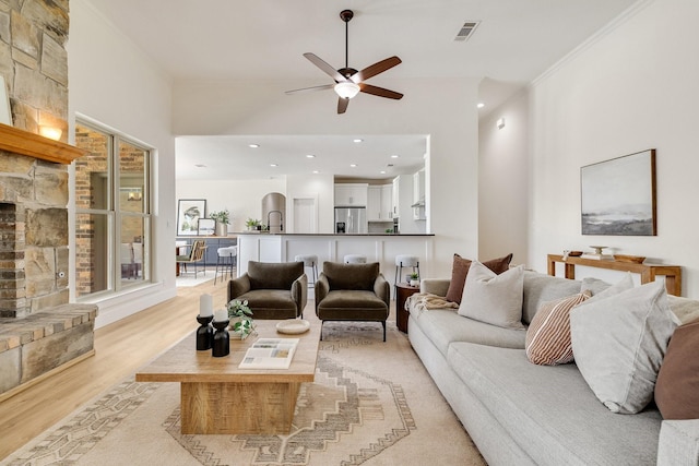 living room featuring visible vents, ceiling fan, light wood-style floors, ornamental molding, and a fireplace