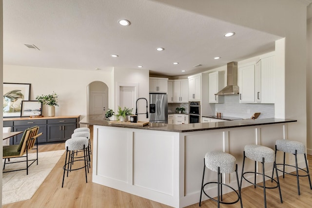 kitchen featuring wall chimney range hood, a breakfast bar area, decorative backsplash, visible vents, and stainless steel appliances