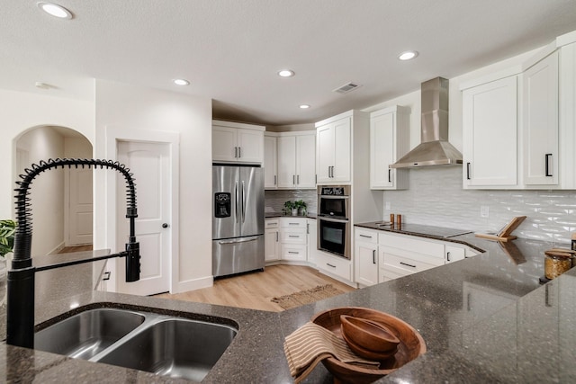 kitchen featuring dark stone counters, stainless steel appliances, a sink, visible vents, and wall chimney exhaust hood