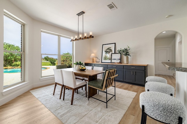 dining area featuring a chandelier, visible vents, baseboards, arched walkways, and light wood-type flooring