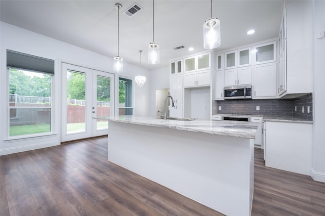 kitchen featuring dark wood finished floors, stainless steel microwave, white cabinets, a sink, and visible vents