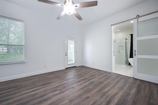 unfurnished bedroom featuring a barn door, access to outside, dark wood-style flooring, ensuite bathroom, and baseboards