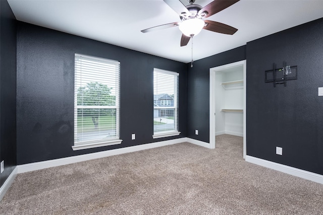 unfurnished bedroom with a closet, carpet, baseboards, a spacious closet, and a ceiling fan