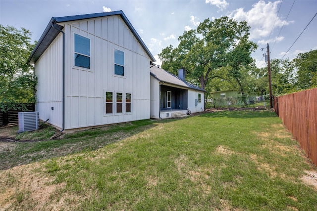 rear view of property with a lawn, central AC, board and batten siding, a chimney, and fence