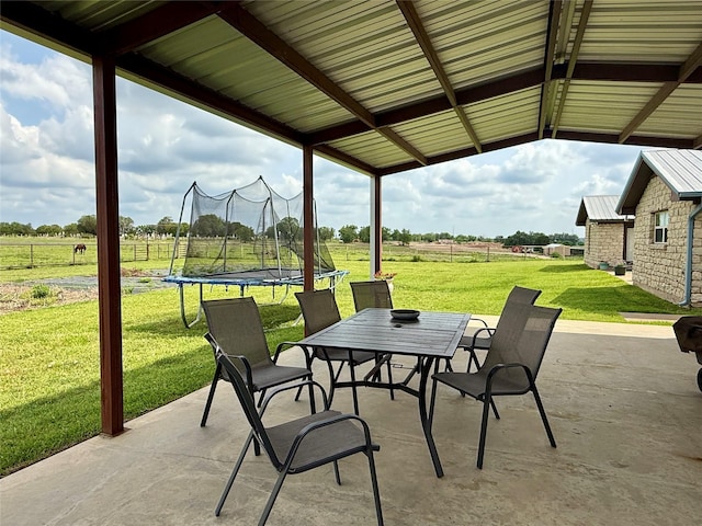 view of patio / terrace with a trampoline, a rural view, and outdoor dining space