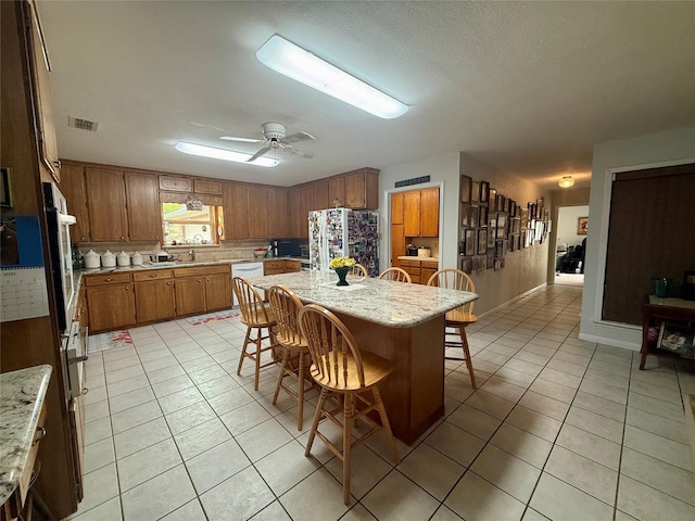 kitchen featuring light tile patterned flooring, a kitchen bar, white appliances, and brown cabinetry