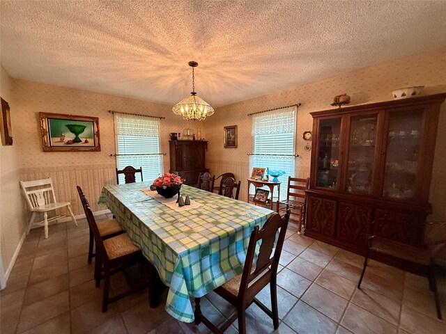 dining space with a chandelier, wallpapered walls, wainscoting, and a textured ceiling