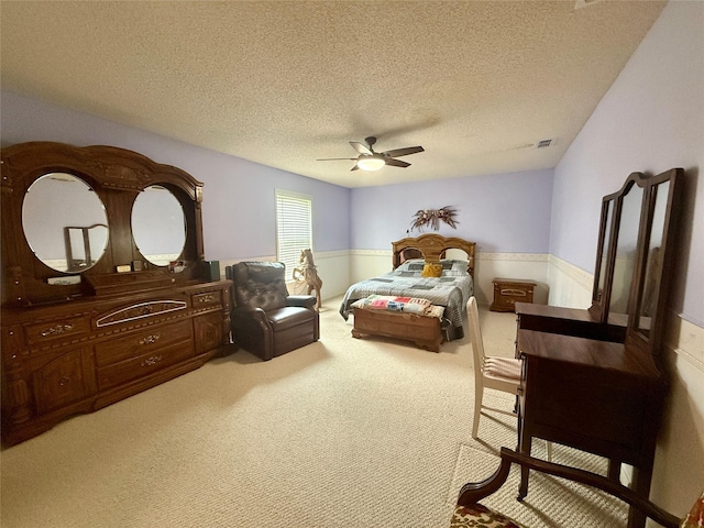 bedroom with carpet flooring, a wainscoted wall, visible vents, a ceiling fan, and a textured ceiling