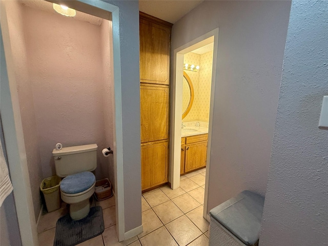 bathroom with toilet, tile patterned flooring, a textured wall, and vanity
