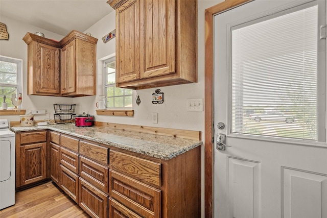clothes washing area featuring washer / clothes dryer, cabinet space, and light wood-style floors
