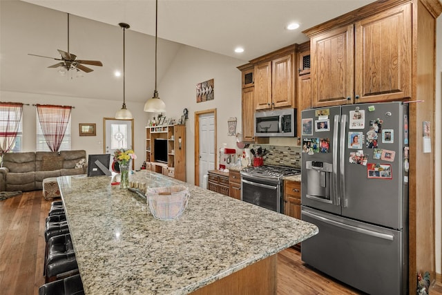kitchen with light stone countertops, stainless steel appliances, ceiling fan, open floor plan, and a kitchen breakfast bar