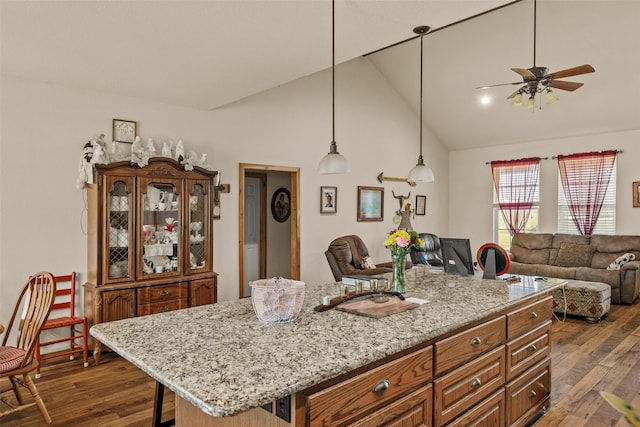 kitchen featuring ceiling fan, dark wood-style flooring, open floor plan, light stone countertops, and brown cabinetry
