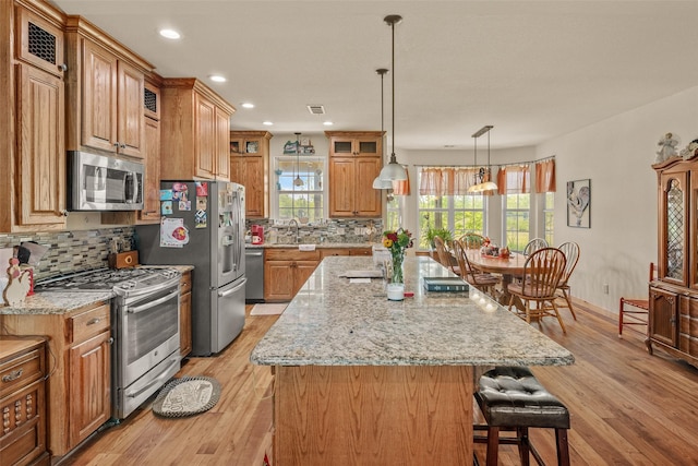 kitchen featuring a kitchen breakfast bar, light wood-style floors, stainless steel appliances, and backsplash