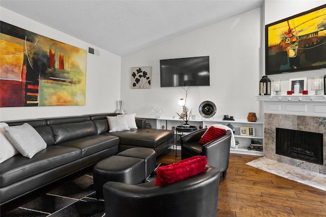living room featuring a textured ceiling, visible vents, a tile fireplace, wood-type flooring, and lofted ceiling